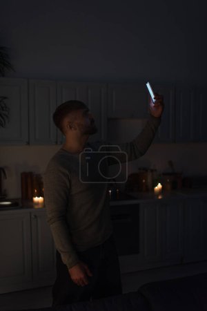 Foto de Hombre sosteniendo el teléfono celular en la mano levantada mientras capta la señal durante el corte de energía - Imagen libre de derechos