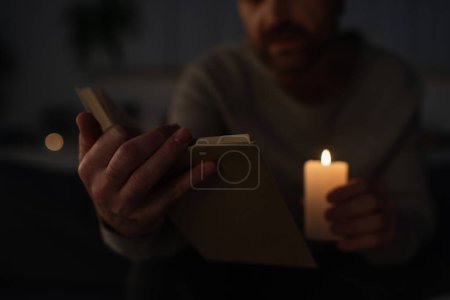 abgeschnittene Ansicht eines Mannes mit brennender Kerze und Lesebuch bei Stromausfall