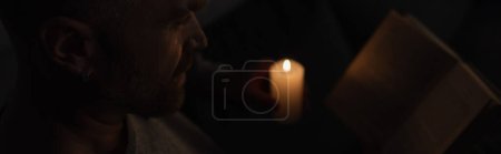 Foto de Hombre leyendo libro cerca de la vela encendida durante el corte de energía en casa, pancarta - Imagen libre de derechos