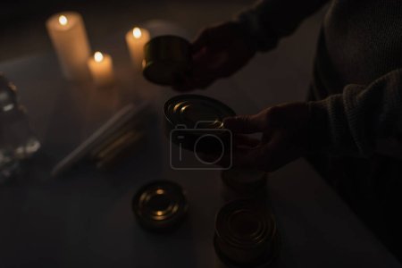 Téléchargez les photos : Vue partielle de l'homme avec de la nourriture en conserve près des bougies brûlant pendant une panne de courant - en image libre de droit