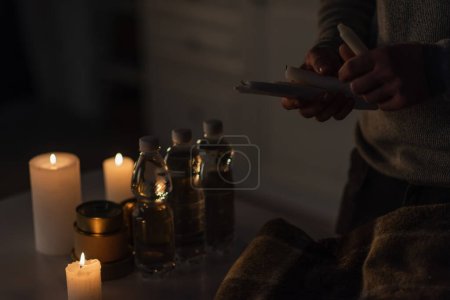 Téléchargez les photos : Vue partielle de l'homme tenant des bougies près de l'eau embouteillée avec des aliments en conserve et une couverture chaude sur la table - en image libre de droit