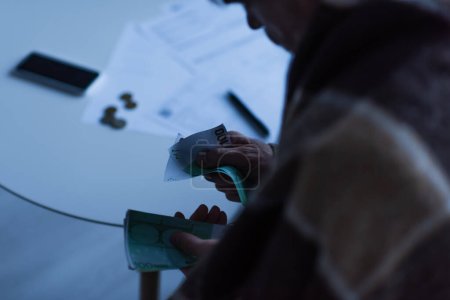 cropped view of man counting money near blurred invoices during electricity outage