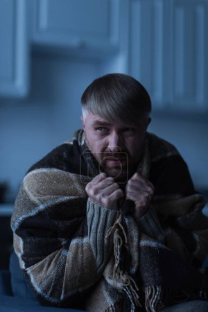 displeased man wrapped in warm blanket and looking away during power blackout
