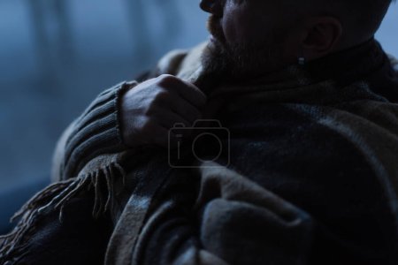 Teilbild eines in eine warme Decke gehüllten Mannes, der während des Stromausfalls zu Hause sitzt