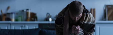 Photo for Frozen man wrapped in blanket warming hands and sitting with bowed head during electricity outage, banner - Royalty Free Image