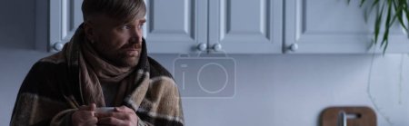 gefrorener Mann in warmer Decke mit heißem Tee in der Hand und in der Dämmerung zu Hause wegschauend, Banner