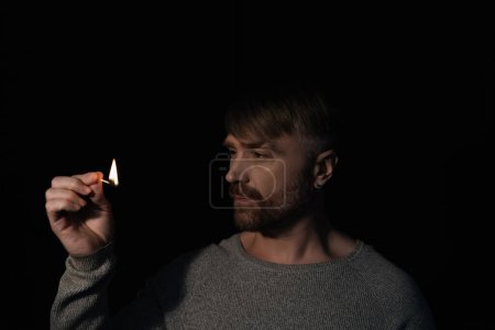 Photo for Man looking at flame of burning match in darkness isolated on black - Royalty Free Image