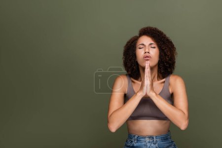 Curly african american woman with closed eyes praying isolated on green 