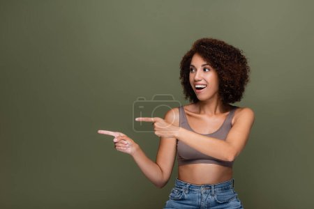 Smiling african american woman pointing with fingers isolated on green 