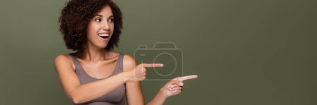 Curly african american model in top pointing with fingers isolated on green, banner 