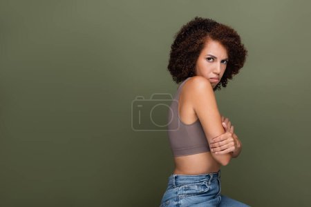 Photo for Embarrassed african american woman in top looking at camera isolated on green - Royalty Free Image
