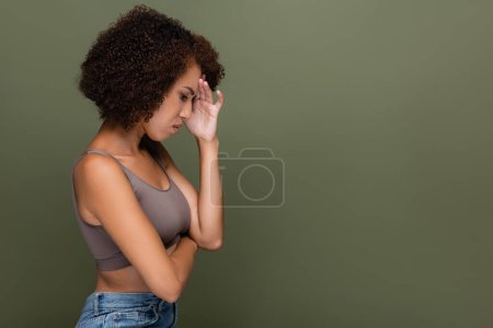 Téléchargez les photos : Vue latérale de femme afro-américaine bouleversée sur le front tactile supérieur isolé sur le vert - en image libre de droit