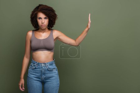Mujer afroamericana seria mostrando gesto de stop y mirando a la cámara aislada en verde 