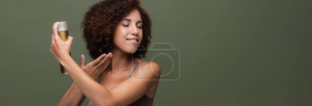 Pretty african american woman applying hairspray isolated on green, banner 