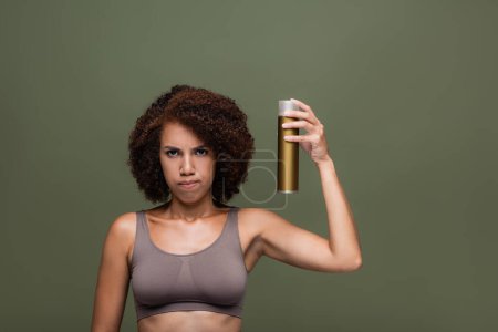 Trauriges afrikanisch-amerikanisches Model im Top mit Haarspray isoliert auf grün 