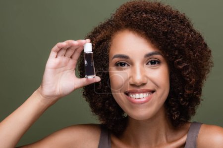 Porträt einer afrikanisch-amerikanischen Frau, die Kosmetiköl auf Grün isoliert hält 