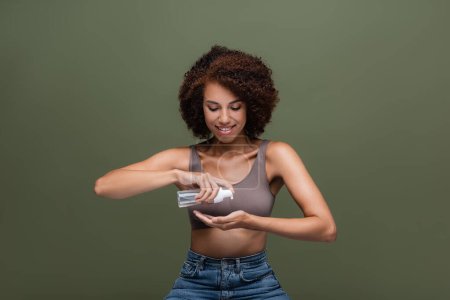 Téléchargez les photos : Femme afro-américaine positive appliquant de la mousse nettoyante sur la main isolée sur vert - en image libre de droit