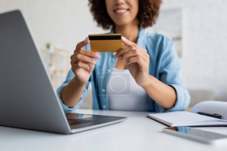 Photo pour Vue recadrée d'une femme afro-américaine floue tenant une carte de crédit près d'appareils - image libre de droit