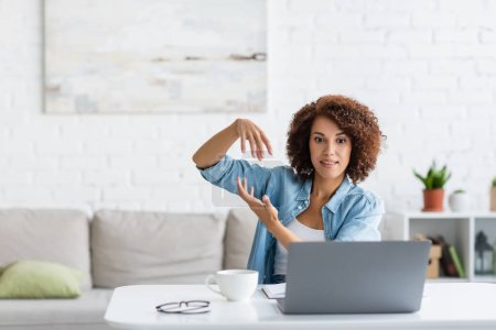 curly african american woman gesturing during video call on laptop 