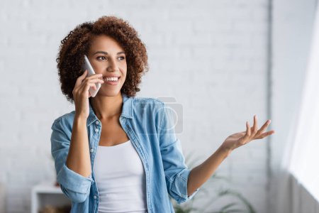 mujer afroamericana feliz hablando en smartphone y haciendo gestos en casa 