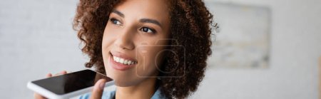 Téléchargez les photos : Femme américaine africaine joyeuse avec cheveux bouclés enregistrement message vocal sur smartphone, bannière - en image libre de droit
