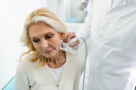 médico haciendo ultrasonido de los ganglios linfáticos en el cuello de la mujer de mediana edad