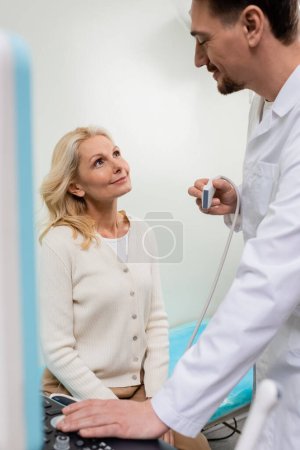glücklicher Arzt mit Ultraschallsonde sieht glückliche blonde Frau im Krankenhaus