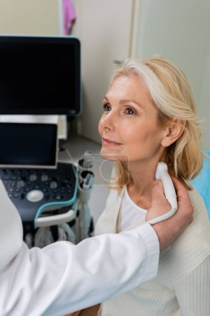 femme blonde souriant près du médecin faisant une échographie de ses ganglions lymphatiques à la clinique