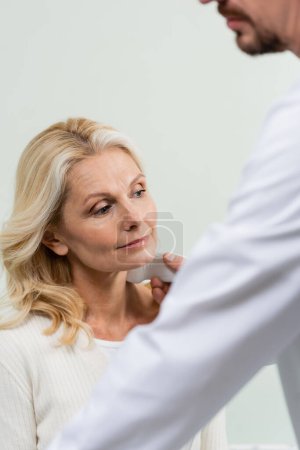 blurred physician doing ultrasound diagnostics of middle aged woman in clinic