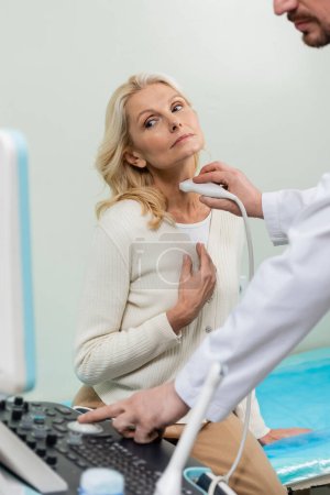 Blonde Frau schaut Ultraschallgerät in der Nähe Arzt macht Diagnose ihres Kehlkopfes