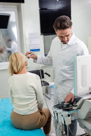Arzt im weißen Kittel justiert Ultraschallgerät, während er die Diagnose einer Frau mittleren Alters durchführt
