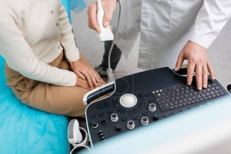 vista recortada del médico que sostiene la sonda de ultrasonido cerca del panel de control y la mujer en la clínica