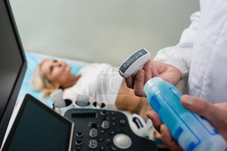Photo for Doctor applying ultrasonic gel on ultrasound probe near patient lying on blurred background - Royalty Free Image