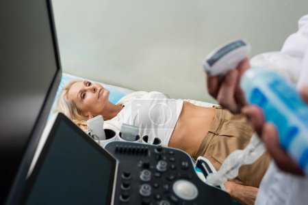 middle aged woman lying near ultrasound machine and physician on blurred foreground