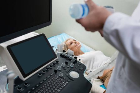 smiling woman lying near doctor preparing ultrasound machine for diagnostics