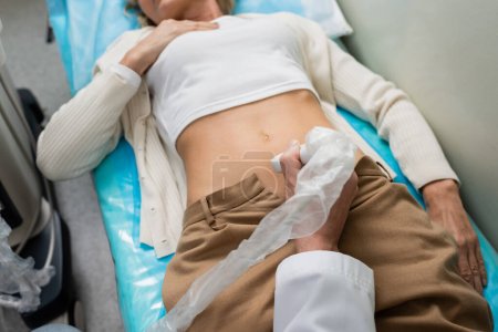 Foto de Vista parcial de la mujer acostada cerca del médico haciendo ultrasonido nefrológico en la clínica - Imagen libre de derechos