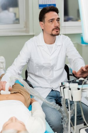 attentive doctor in white coat doing kidneys ultrasound of patient in clinic