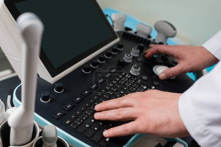 vue recadrée du médecin opérant la machine ultrasonore moderne avec écran blanc