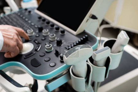vista parcial del médico utilizando el panel de control de la máquina de ultrasonido en el hospital