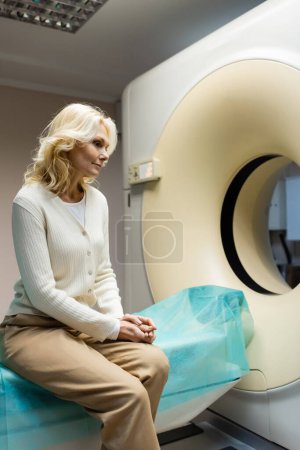 pensive middle aged woman sitting near ct scanner in hospital