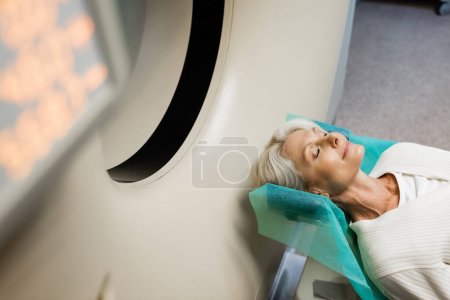 Hochwinkelaufnahme einer reifen Frau mit geschlossenen Augen bei der Diagnostik am CT-Scanner auf verschwommenem Vordergrund