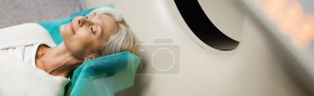 Photo for High angle view of mature woman with closed eyes lying during diagnostics on ct scanner in clinic, banner - Royalty Free Image