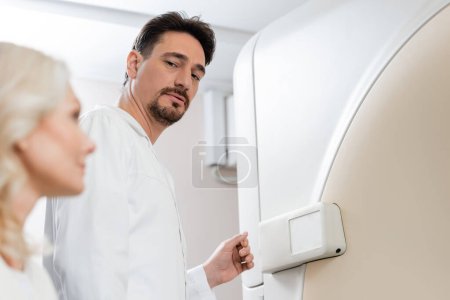 serious radiologist looking at blurred middle aged woman near ct scanner in hospital