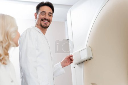 vista de ángulo bajo del radiólogo sonriente mirando a la mujer borrosa cerca de la máquina de tomografía computarizada