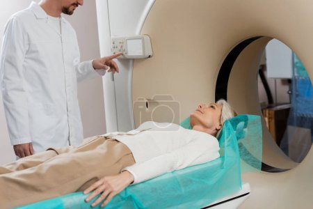 Frau mittleren Alters liegt während der Diagnostik in der Nähe von Arzt, der CT-Scanner operiert