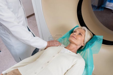 mujer sonriente mirando al radiólogo tocándose el hombro antes de escanear en la máquina de tomografía computarizada
