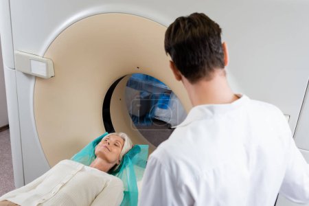 Foto de Médico morena de pie cerca de la mujer durante el diagnóstico en el escáner de tomografía computarizada - Imagen libre de derechos