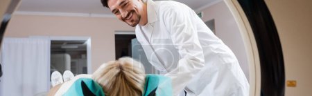 radiologist in white coat smiling near woman and computed tomography machine, banner