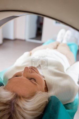 Photo for Mature woman with closed eyes lying during diagnostics on ct scanner on blurred background - Royalty Free Image