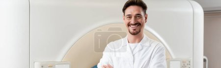 alegre médico sonriendo a la cámara mientras está de pie cerca del escáner de tomografía computarizada, pancarta